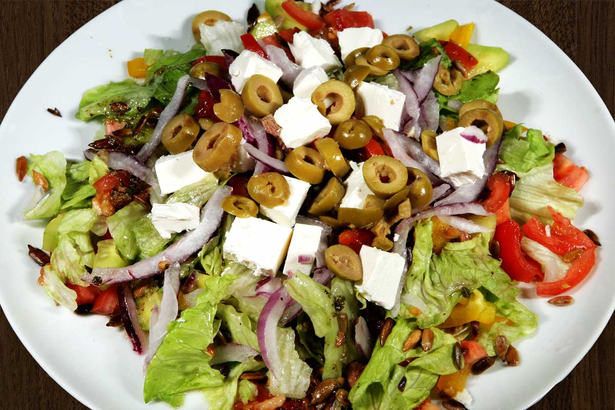 A composition of fresh vegetables with salad and sandwich cheese, Greek olives and vinaigrette sauce